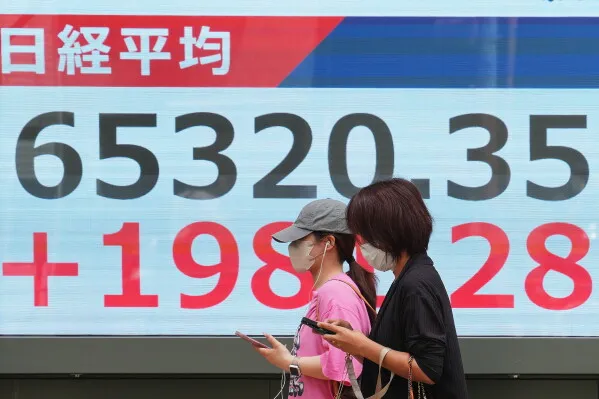 امرأتان ترتديان أقنعة واقية تسيران بجانب شاشة تعرض مؤشر Nikkei 225 الياباني، مع ارتفاعه بمقدار 198.28 نقطة.