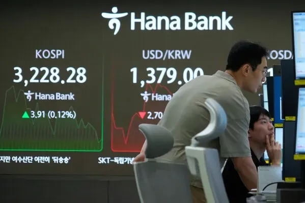 شخصان يتابعان شاشة تداول في بنك هانا، تعرض مؤشرات كوسبي وسعر الدولار مقابل الوون الكوري، مع تحركات طفيفة في السوق.