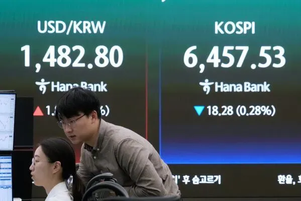 شخصان يتابعان شاشات التداول في بورصة كورية، مع عرض أسعار الدولار الأمريكي مقابل الوون الكوري ومؤشر كوسبي، في سياق أداء الأسواق الآسيوية.