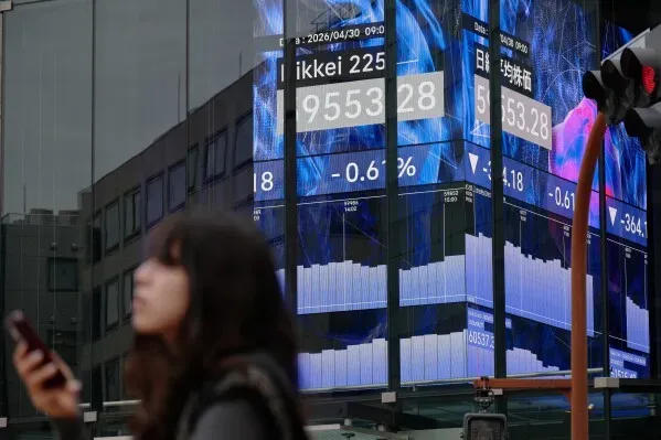 شاشة تعرض بيانات مؤشر Nikkei 225 في طوكيو، مع امرأة تحمل هاتفًا، تعكس تذبذبات السوق وسط ارتفاعات في الأسهم وأسعار النفط.