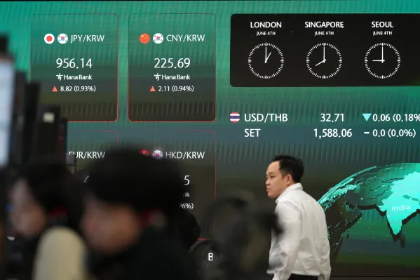 تظهر الشاشة المالية في سوق العملات مع بيانات عن أسعار الصرف، بينما يتواجد متداولون في الخلفية.
