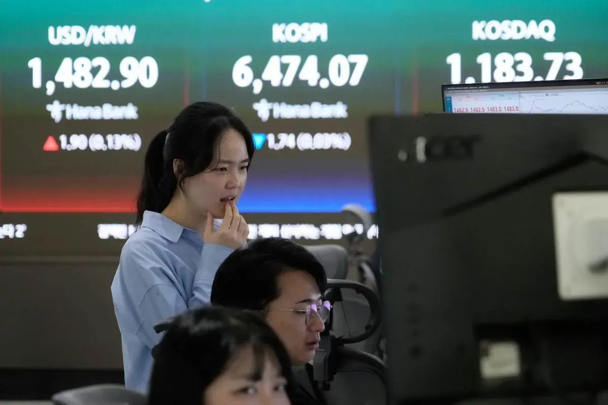 امرأة تراقب شاشات التداول في سوق الأسهم، مع عرض أسعار العملات ومؤشرات الأسهم مثل KOSPI وKOSDAQ في الخلفية، تعكس تباين الأسواق الآسيوية.