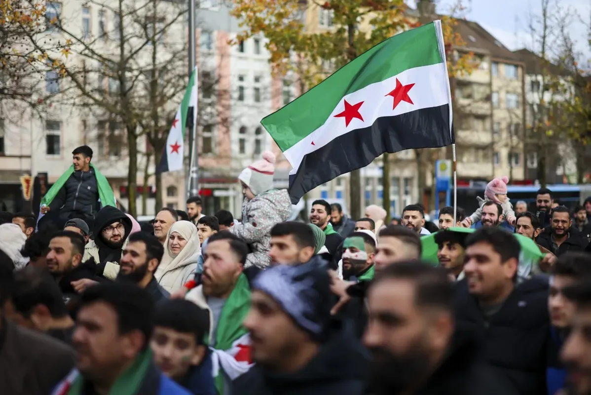 محتجون يحملون علم الثورة السورية خلال تجمع في مدينة ألمانية، يعبرون عن دعمهم للاجئين السوريين في ظل الأزمات المستمرة.