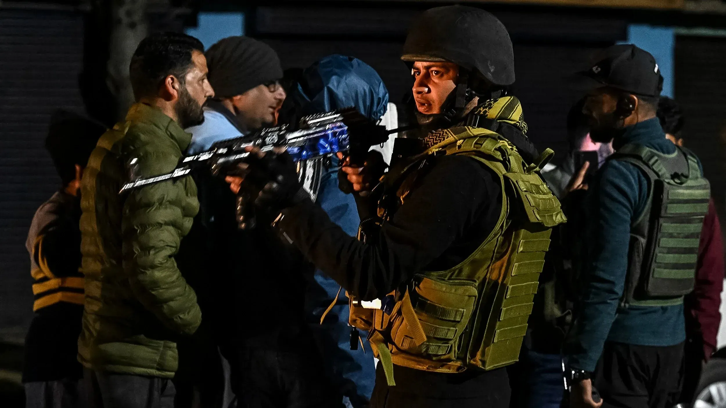 عناصر أمنية مسلحة في كشمير خلال حالة طوارئ بعد هجوم على سياح، مع وجود أشخاص في الخلفية يعبرون عن القلق.