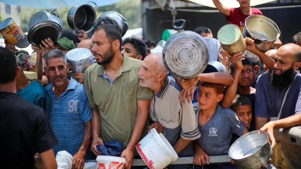 تجمع حشد من الفلسطينيين في غزة للحصول على المساعدات الغذائية، حاملين أوعية فارغة، وسط أجواء من التوتر والقلق.