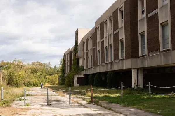 منطقة مشجرة خلف مدرسة مهجورة حيث عُثر على رفات كادا سكوت، مع وجود شخص في المسافة بالقرب من المبنى.