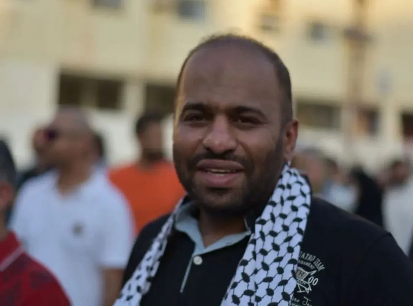 ناشط حقوقي بحريني، علي الحاجي، يتوسط حشد من الناس، يرتدي كوفية، في سياق احتجاجات تطالب بحقوق الإنسان.