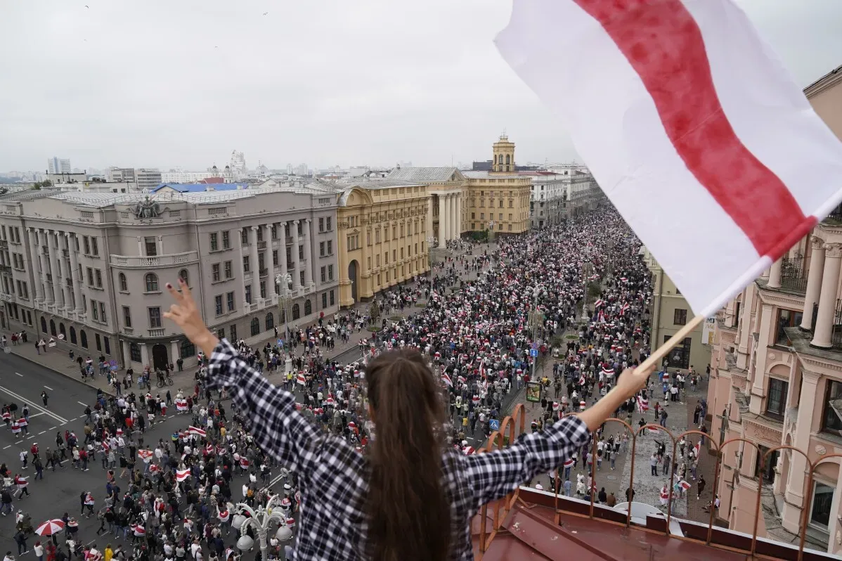 شخصية ترفع علم بيلاروسيا الأبيض والأحمر، بينما تتجمع حشود كبيرة من المحتجين في وسط المدينة خلال مظاهرة ضد النظام.