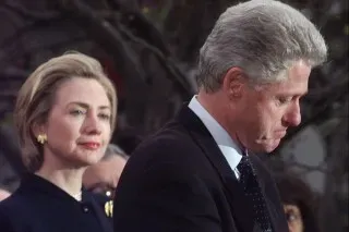 بيل وهيلاري كلينتون في لحظة تأمل، حيث يظهر بيل وهو ينظر إلى الأسفل بينما تراقبه هيلاري، مما يعكس التوترات السياسية الحالية.