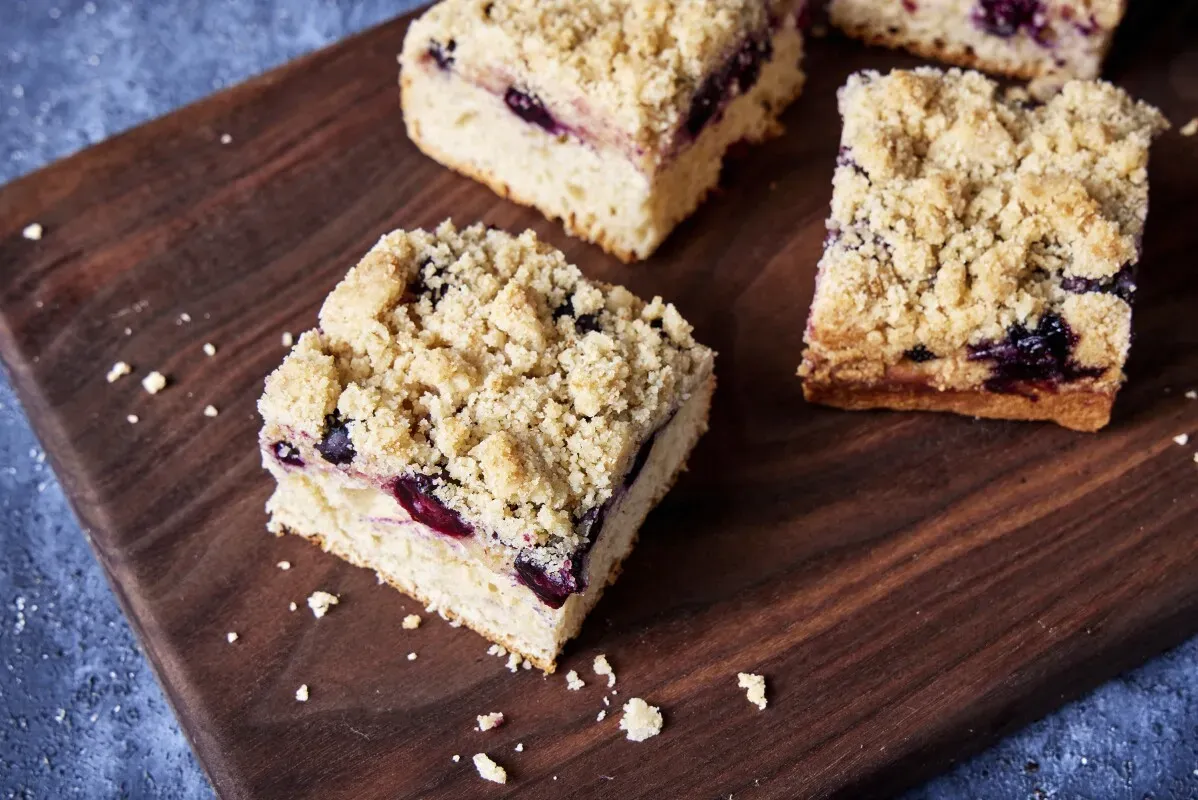 كعكة ستريوسل الألمانية تحتوي على طبقة من التوت الأزرق، مغطاة بستريوسيل مقرمش، موضوعة على لوح خشبي.