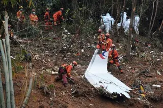 فرق الإنقاذ تعمل في موقع تحطم طائرة China Eastern Airlines في منطقة جبلية، مع وجود حطام الطائرة وسط الأشجار.