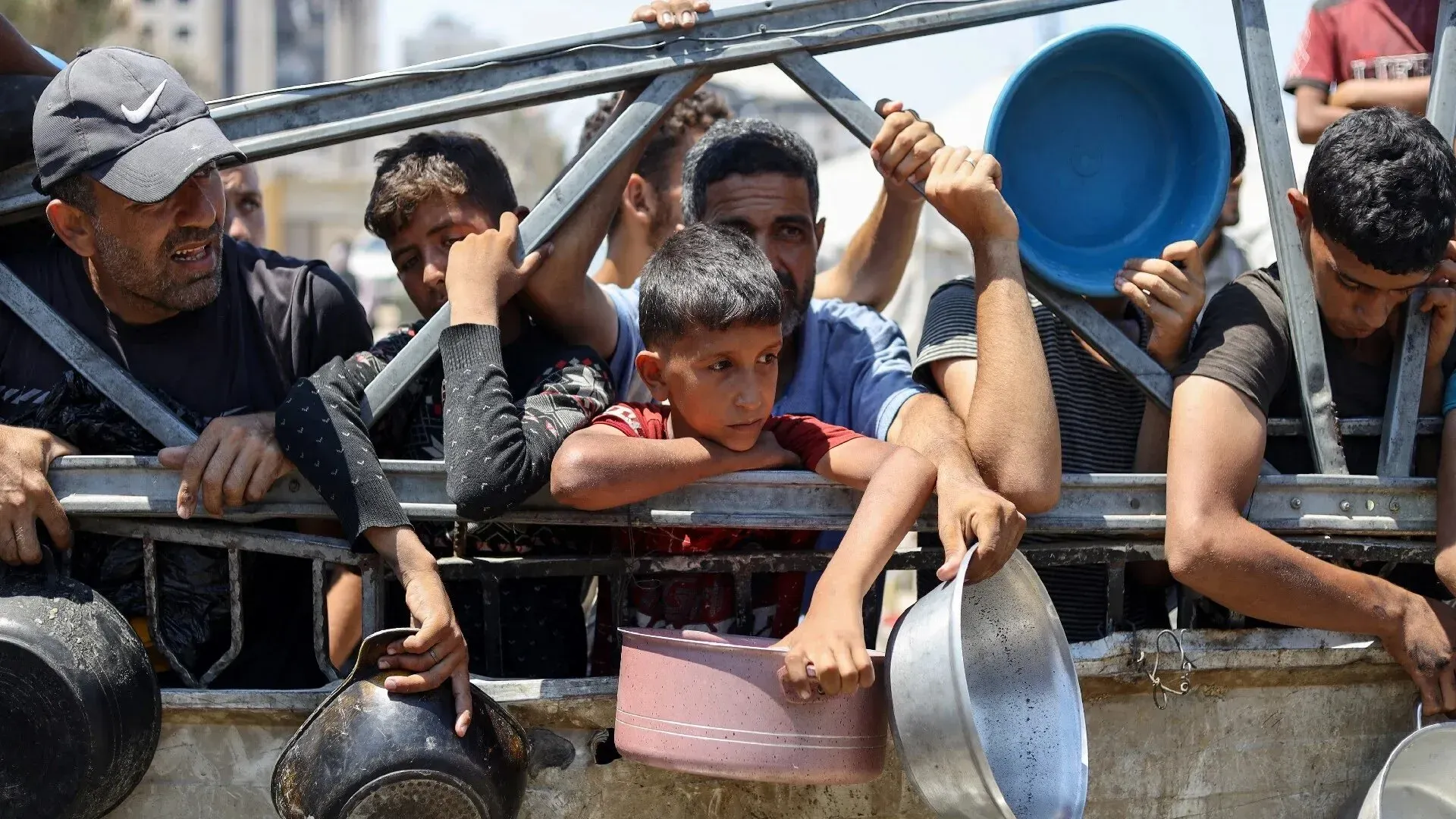 رجال وأطفال فلسطينيون يتجمعون حول حاجز للحصول على المساعدات الإنسانية، مع تزايد المعاناة بسبب الحصار في غزة.