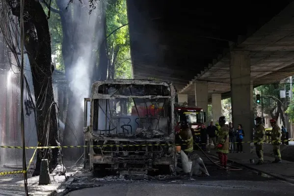 حافلة محترقة في ريو دي جانيرو بعد هجوم من مهربي المخدرات، مع وجود رجال إطفاء في الموقع. تعكس الصورة حالة الفوضى والذعر في المنطقة.