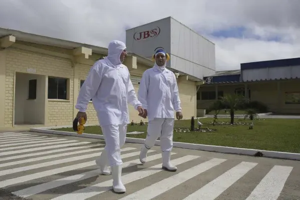 عمال في شركة JBS للبروتينات الحيوانية يرتدون ملابس واقية أثناء توجههم إلى منشأة الإنتاج، مما يعكس صناعة اللحوم المعقدة.