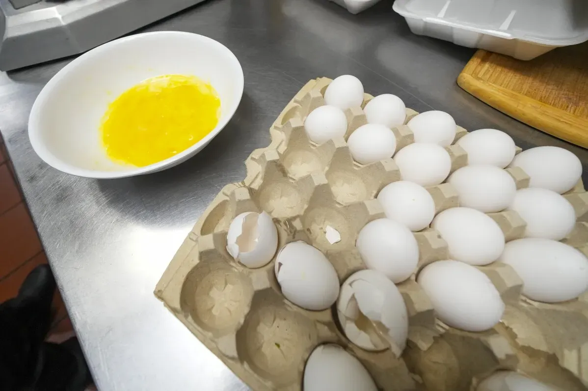 بيض في علبة كرتونية مع بيضة مكسورة وصحن يحتوي على صفار البيض، تعكس زيادة الطلب على البيض في المطاعم الأمريكية.