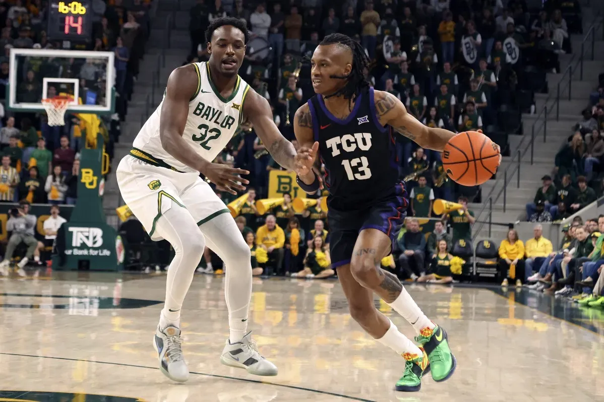 لاعب كرة سلة من فريق TCU يتجاوز دفاع لاعب بايلور في مباراة حماسية، مع مشجعين في الخلفية. تشير التفاصيل إلى ترقب الشوط الثاني.