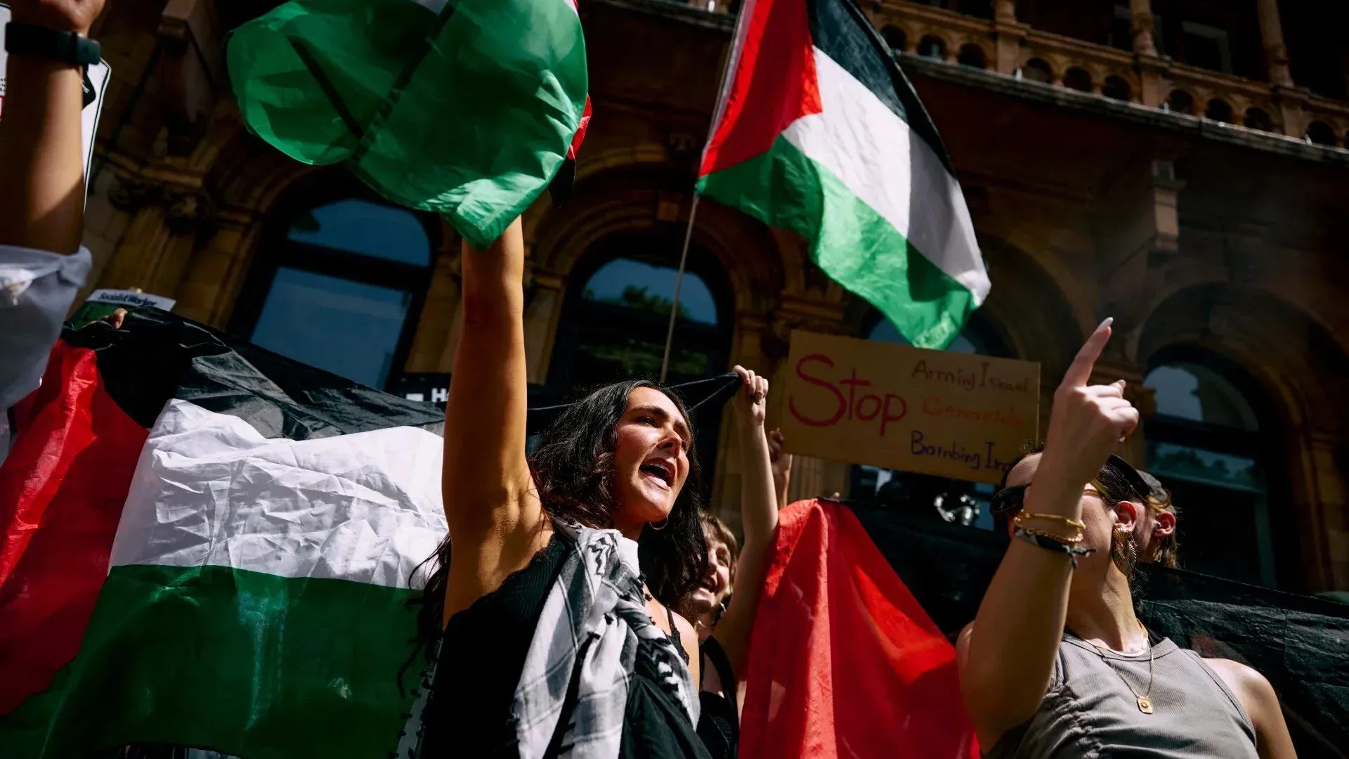 محتجون يحملون الأعلام الفلسطينية في تظاهرة ضد العنف في غزة، مع لافتة تطالب بوقف القصف، تعبيرًا عن دعمهم للحقوق الإنسانية.
