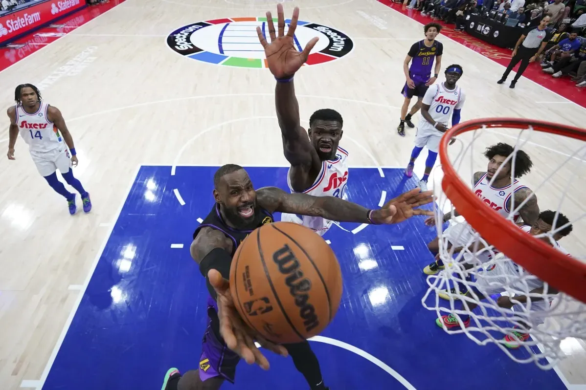 لاعب ليكرز ليبرون جيمس يسجل سلة مرتفعة بينما يحاول لاعب 76ers إيقافه، مع وجود لاعبين آخرين في الخلفية.