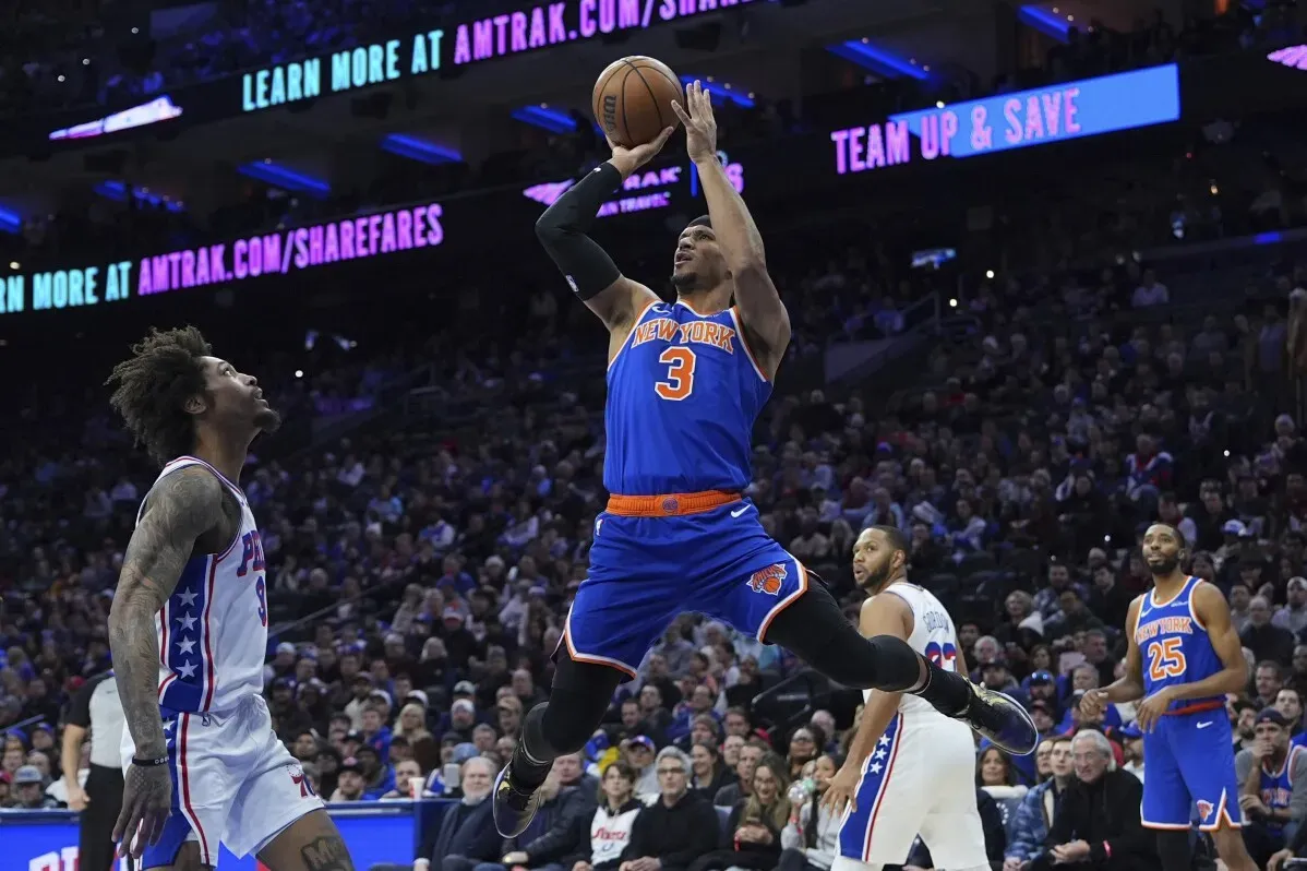 لاعب كرة سلة من فريق نيكس يقوم بتسديد الكرة أثناء المباراة ضد فيلادلفيا 76ers، مع تواجد لاعبين آخرين في الخلفية.