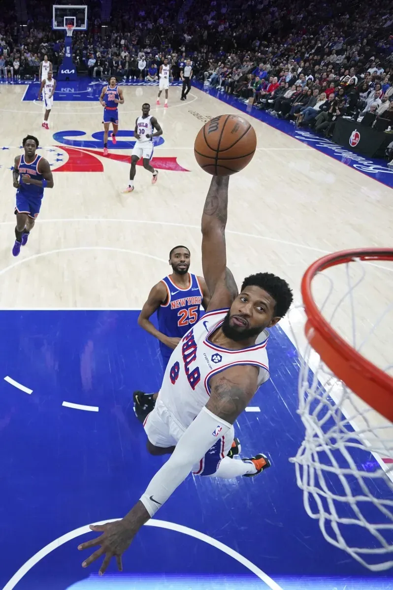 لاعب من فريق 76ers يسجل نقطة بإحدى السلات خلال مباراة ضد نيكس، مع وجود لاعبين آخرين في الخلفية.