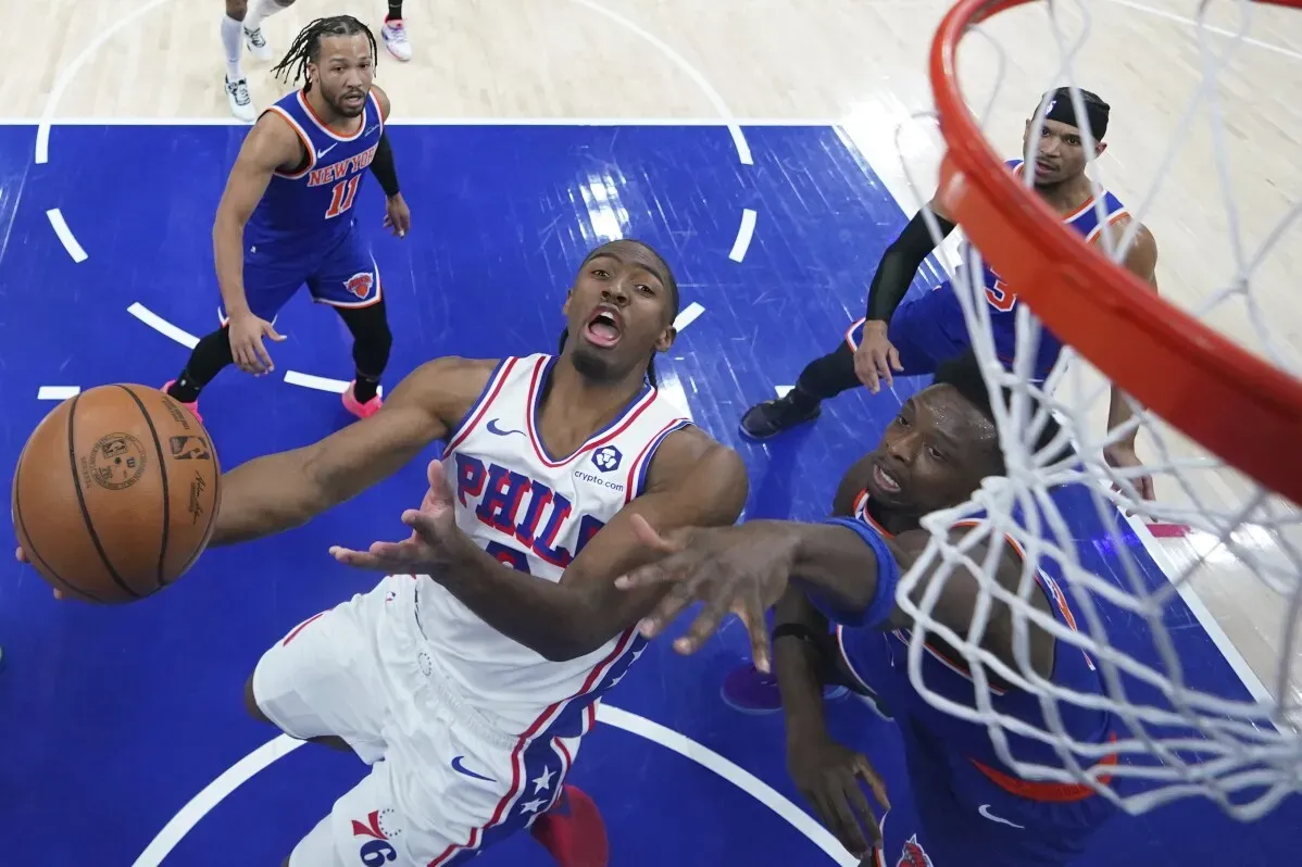 لاعب من فريق فيلادلفيا 76ers يحاول تسجيل نقطة بينما يتصدى له لاعبان من فريق نيويورك نيكس في مباراة مثيرة.
