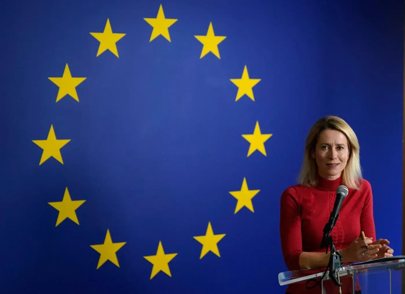 تظهر المسؤولة السياسية الأوروبية Kaja Kallas تتحدث أمام خلفية علم الاتحاد الأوروبي، معبرة عن مواقف الاتحاد في الأزمات العالمية.