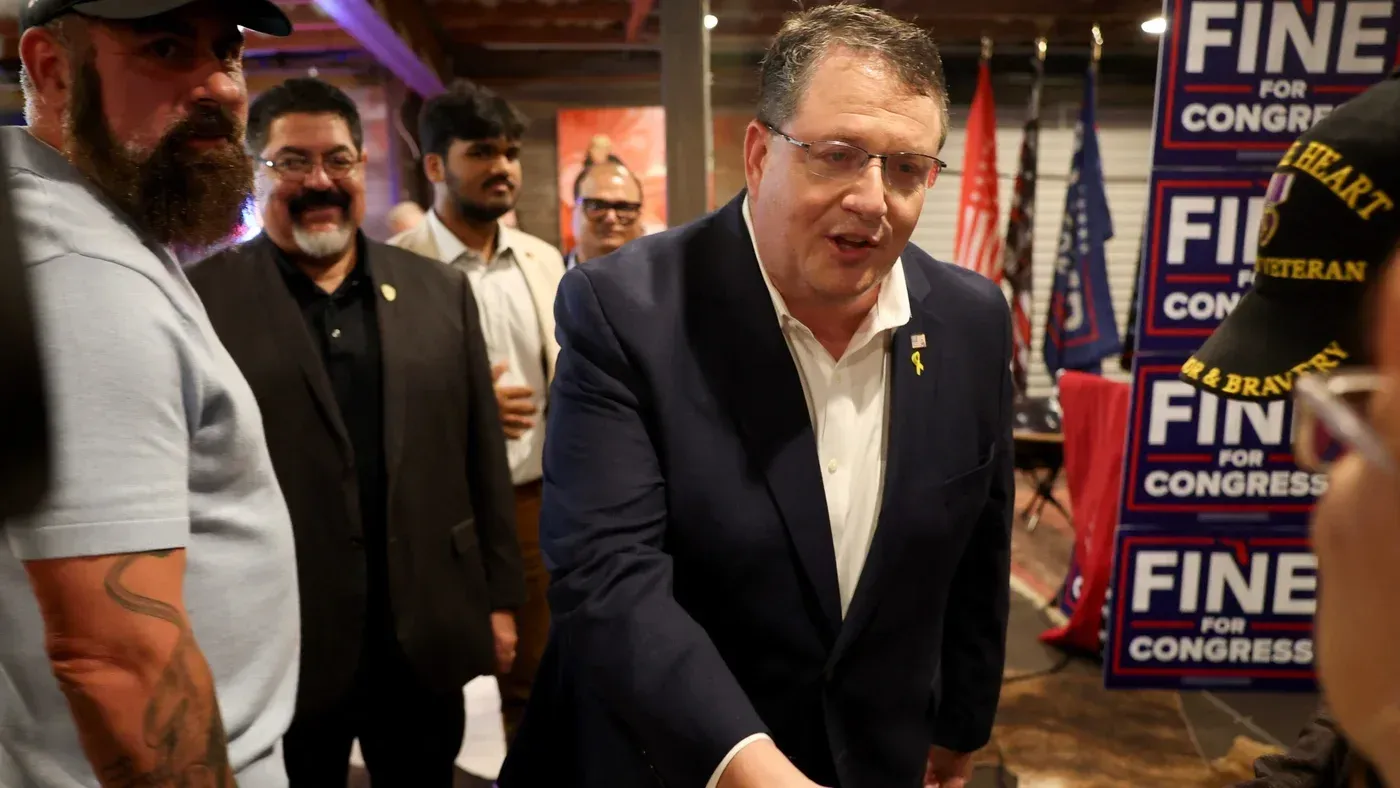 راندي فاين، النائب الجمهوري، يتحدث مع مؤيديه خلال حدث انتخابي، مع لافتات تدعمه في الخلفية.