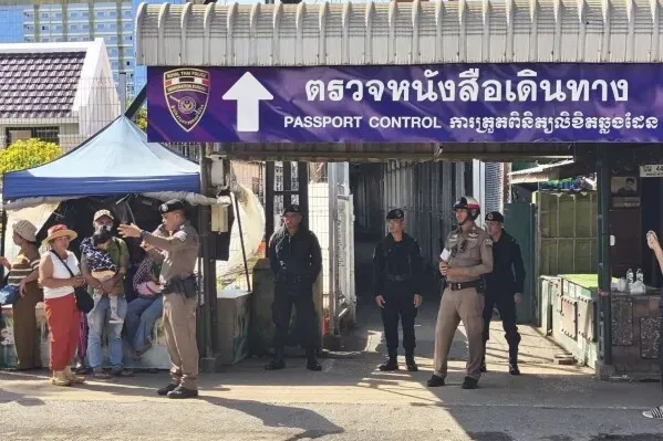 تظهر الصورة نقطة تفتيش جوازات السفر على الحدود بين تايلاند وكمبوديا، مع وجود عناصر أمنية وركاب ينتظرون العبور.