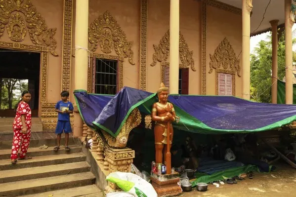 أطفال يقفون بجوار معبد في كمبوديا، حيث يستخدمون كملجأ من النزاع، مع تمثال يرمز للسلام في الخلفية.