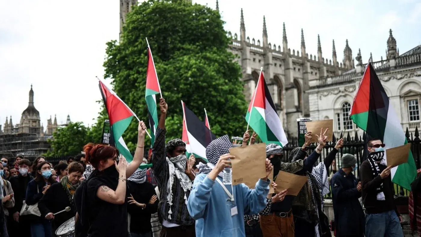 تجمع حشود من المتظاهرين في جامعة كامبريدج حاملين الأعلام الفلسطينية، مع تواجد لافتات تعبر عن دعمهم للقضية الفلسطينية.