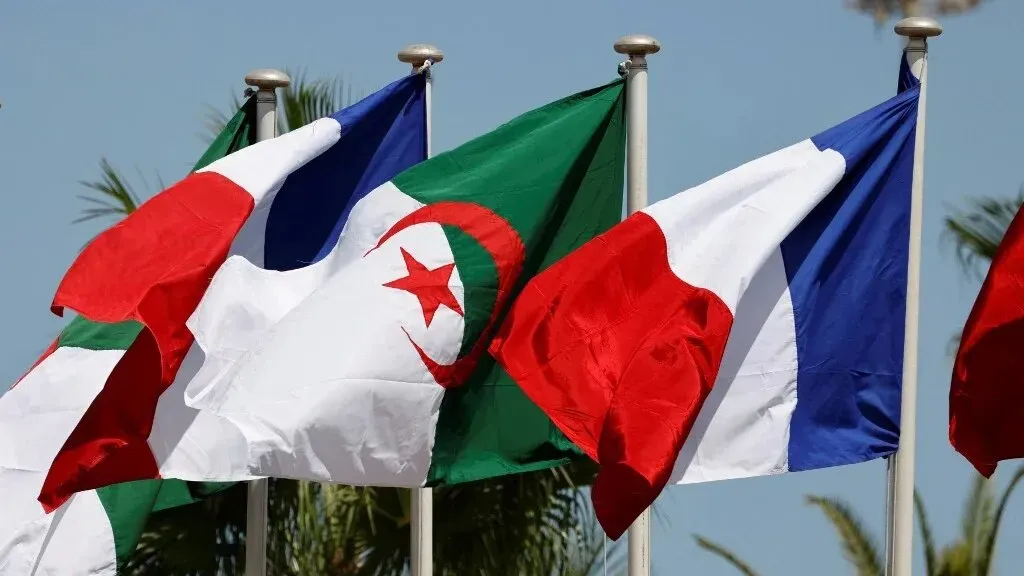 أعلام الجزائر وفرنسا وإيطاليا ترفرف معًا، تعكس التوترات الدبلوماسية بين الجزائر وفرنسا في سياق تاريخي معقد.