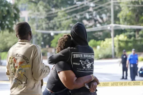 محتجون يتعانقون في موقع حادث إطلاق نار قرب مركز مكافحة الأمراض والوقاية منها، مع وجود عناصر أمنية في الخلفية.
