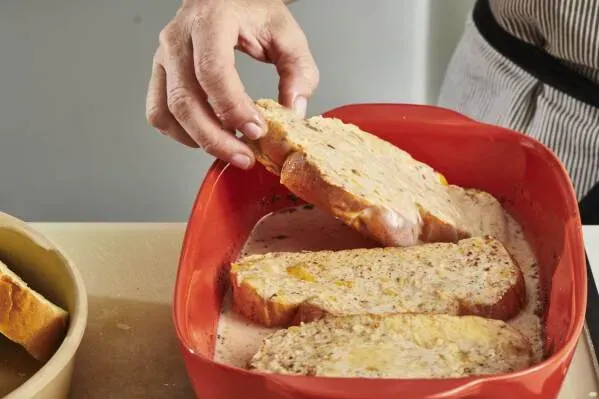 شرائح من الخبز تُغمس في خليط البيض والحليب، جاهزة لتحضير الخبز الفرنسي المحمص، مع التركيز على القوام الغني.