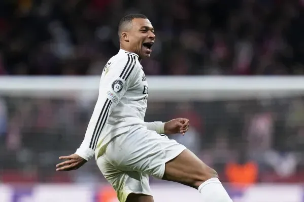كيليان مبابي يحتفل بتسجيل هدف خلال مباراة دوري أبطال أوروبا، مرتديًا زي ريال مدريد، مع أجواء حماسية في الملعب.