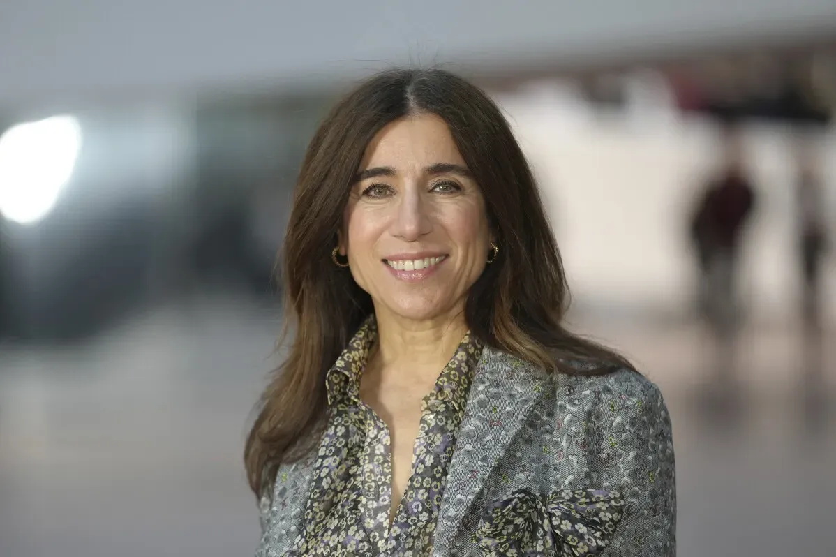مديرة شانيل الجديدة ماثيو بلازي مبتسمة، ترتدي سترة مزينة وأقراط دائرية، مع خلفية مضاءة وقاعة عرض مزدحمة.
