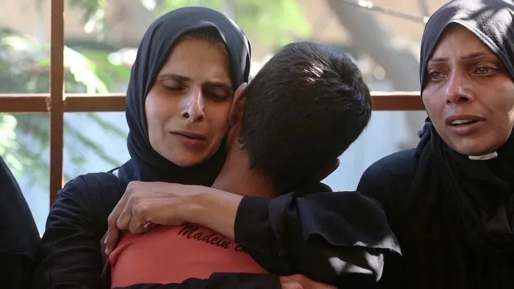 أم فلسطينية تحتضن طفلًا، تعبر عن مشاعر الحزن والقلق بعد الإفراج عن الأطفال المعتقلين، وسط أجواء مؤلمة في غزة.