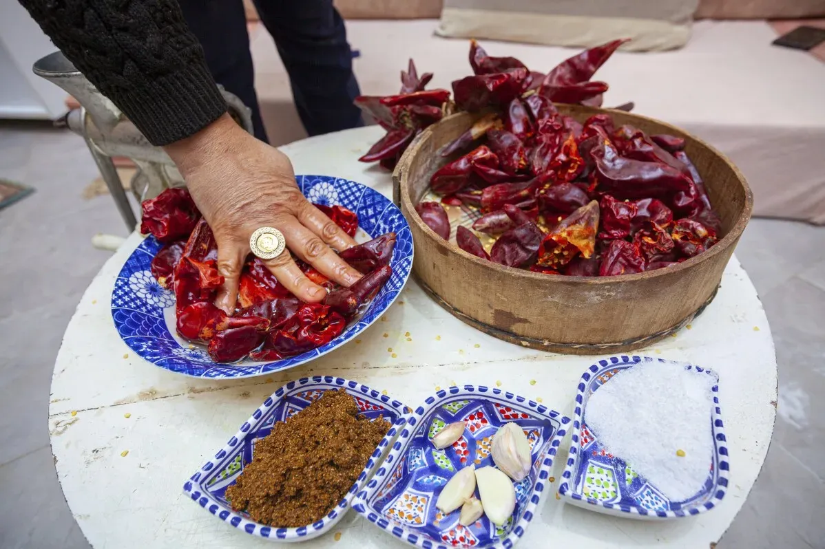 يد تظهر وهي تضع الفلفل الأحمر الجاف في طبق، مع توابل وثوم وملح، في إطار تحضير الهريسة التونسية الشهيرة.