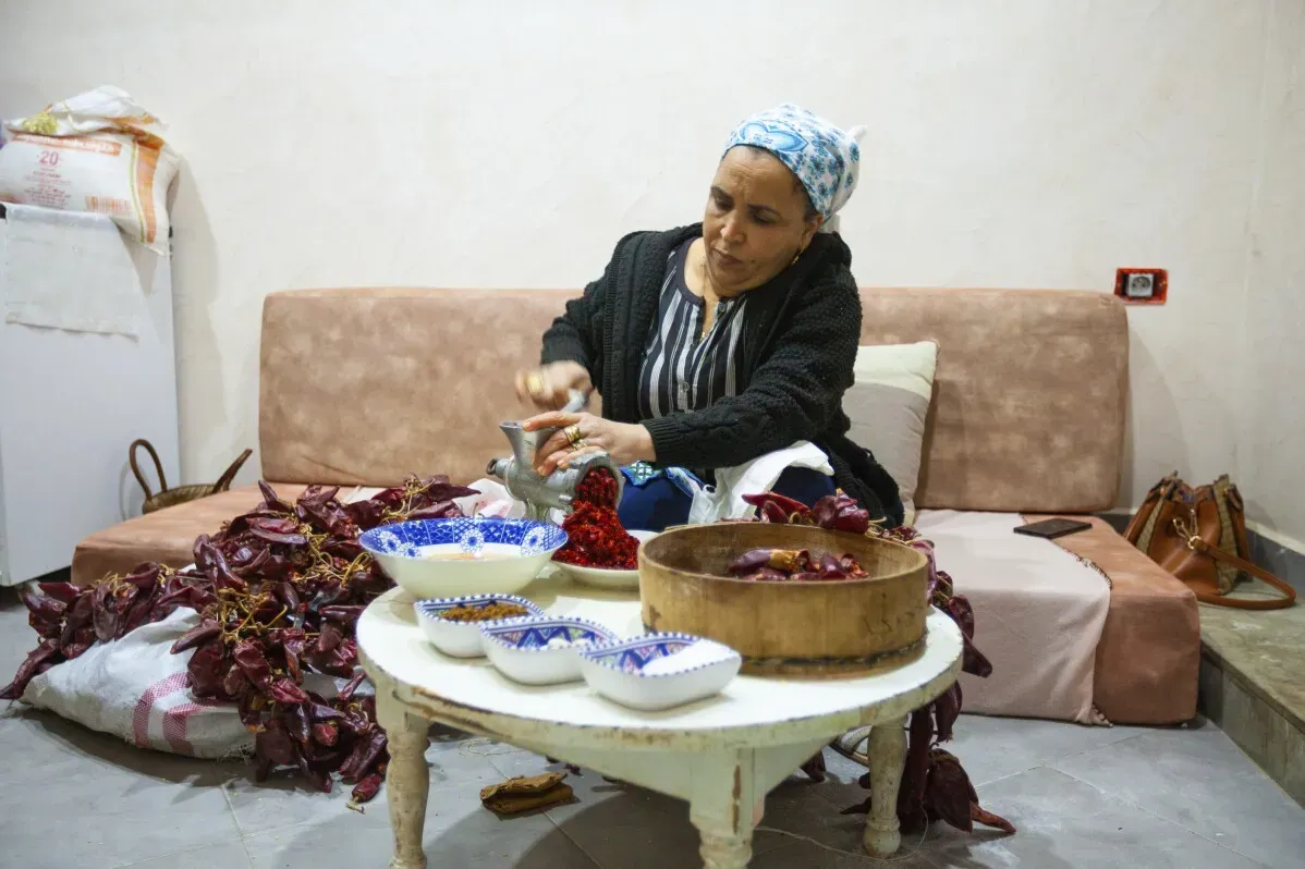 امرأة تونسية تحضر الهريسة، محاطة بالفلفل الأحمر المجفف، تعمل على طحن المكونات في هاون، تعبير عن التراث الثقافي التونسي.