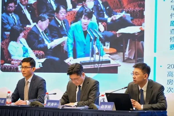 اجتماع رسمي في الصين يتضمن ثلاثة متحدثين، مع صورة خلفية لامرأة تتحدث في مؤتمر، تعكس التوترات بين الصين واليابان.