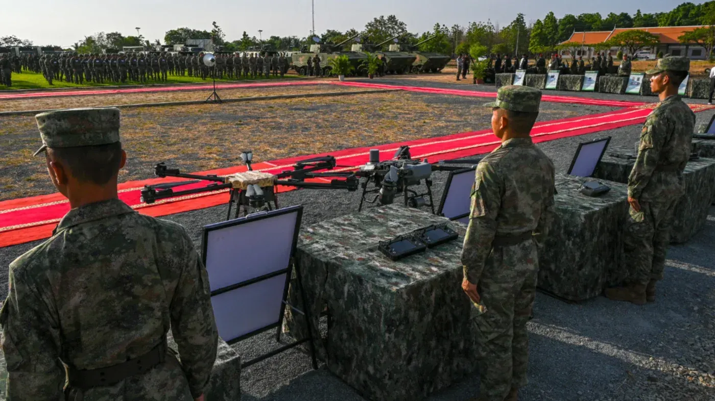 تجمع عسكري يظهر جنودًا يرتدون زيًا رسميًا أمام طاولات تحتوي على أسلحة وذخائر، مما يشير إلى تسليم أسلحة هجومية ودفاعية لإيران.