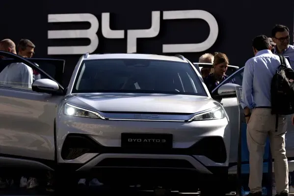سيارة BYD Atto 3 الكهربائية الجديدة مع أبواب مفتوحة، في معرض للسيارات، مع وجود زوار يتفقدونها، خلفها شعار BYD.
