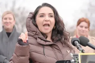 النائبة ديليا راميريز تتحدث خلال مؤتمر صحفي، داعيةً لحظر استخدام جهاز WRAP في عمليات الترحيل، مع وجود مؤيدين خلفها.