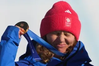 شارلوت بانكس تحتفل بفوزها بالميدالية الذهبية في التزلج على الجليد المختلط، مرتدية قبعة حمراء، مع تعبير عن الفرح.