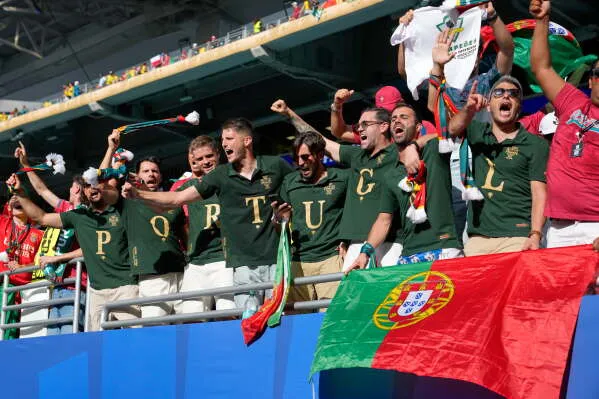 مشجعو البرتغال يحتفلون في ملعب Miami Stadium، يرتدون قمصاناً تحمل حرف "P" ويهتفون بشغف لدعم فريقهم خلال مباراة كأس العالم.