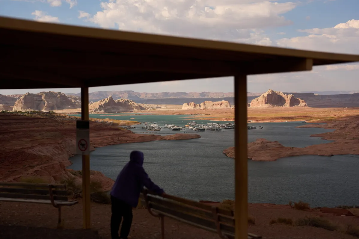 شخص يقف تحت مظلة مطلة على نهر Colorado ومنحدرات صخرية جافة، تعكس أزمة نقص المياه في غرب الولايات المتحدة.
