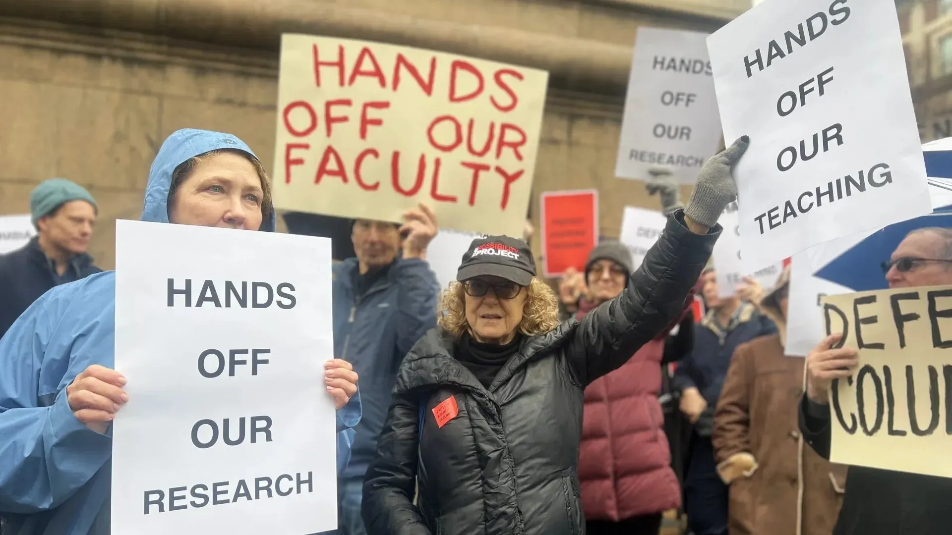 احتجاج لأعضاء هيئة التدريس في جامعة كولومبيا، يحملون لافتات تدعو للدفاع عن البحث والتعليم، وسط أجواء باردة وممطرة.