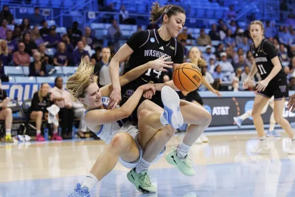 لاعبة كرة سلة من واشنطن تتصارع مع لاعبة من كولومبيا على الكرة خلال مباراة NCAA، مع أجواء حماسية في الملعب.