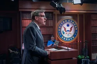 تظهر الصورة السيناتور مارك وارنر يتحدث في قاعة مجلس الشيوخ الأمريكي، مع شعار الولايات المتحدة خلفه، أثناء مناقشة قضايا الاستخبارات.