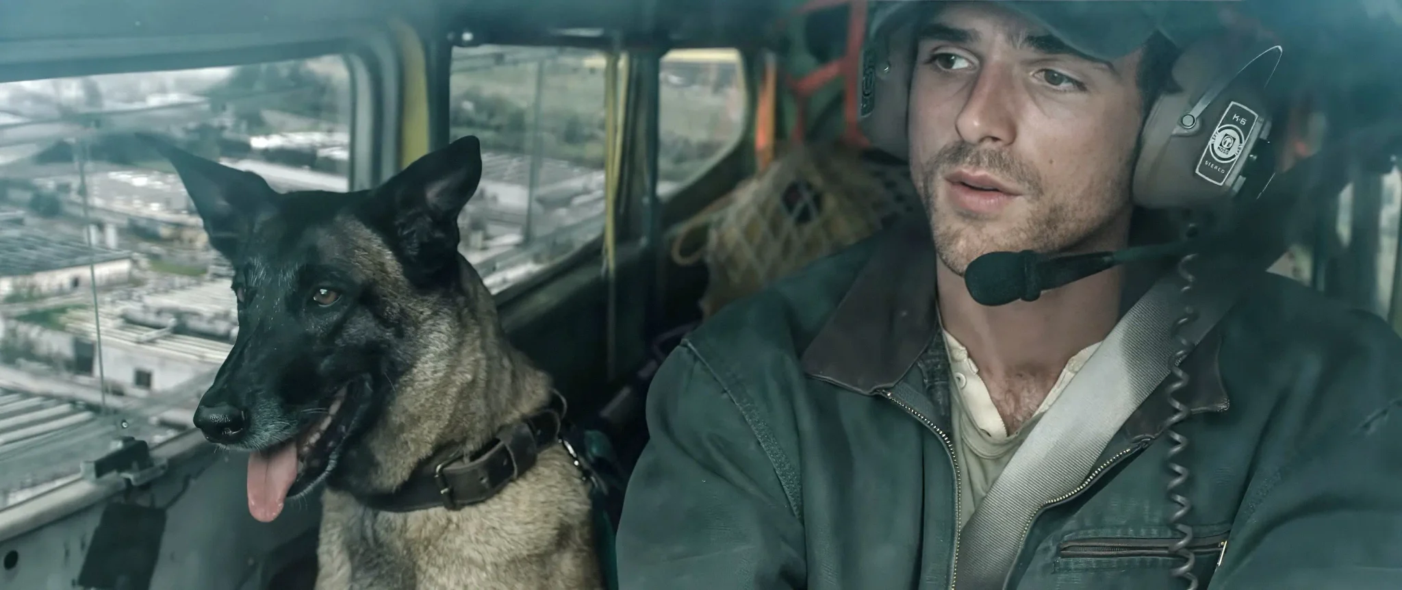 شاب يرتدي سماعة رأس يقود طائرة صغيرة برفقة كلبه، مشهد من فيلم The Dog Stars بعد الوباء يعكس الوحدة والصمت.