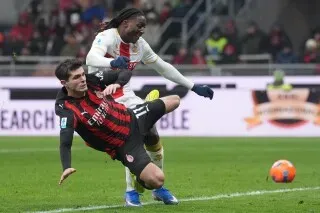 لاعبان يتنافسان على الكرة في مباراة كرة قدم، حيث يظهر أحدهما وهو يسقط أرضًا بينما يحاول الآخر السيطرة على الكرة.